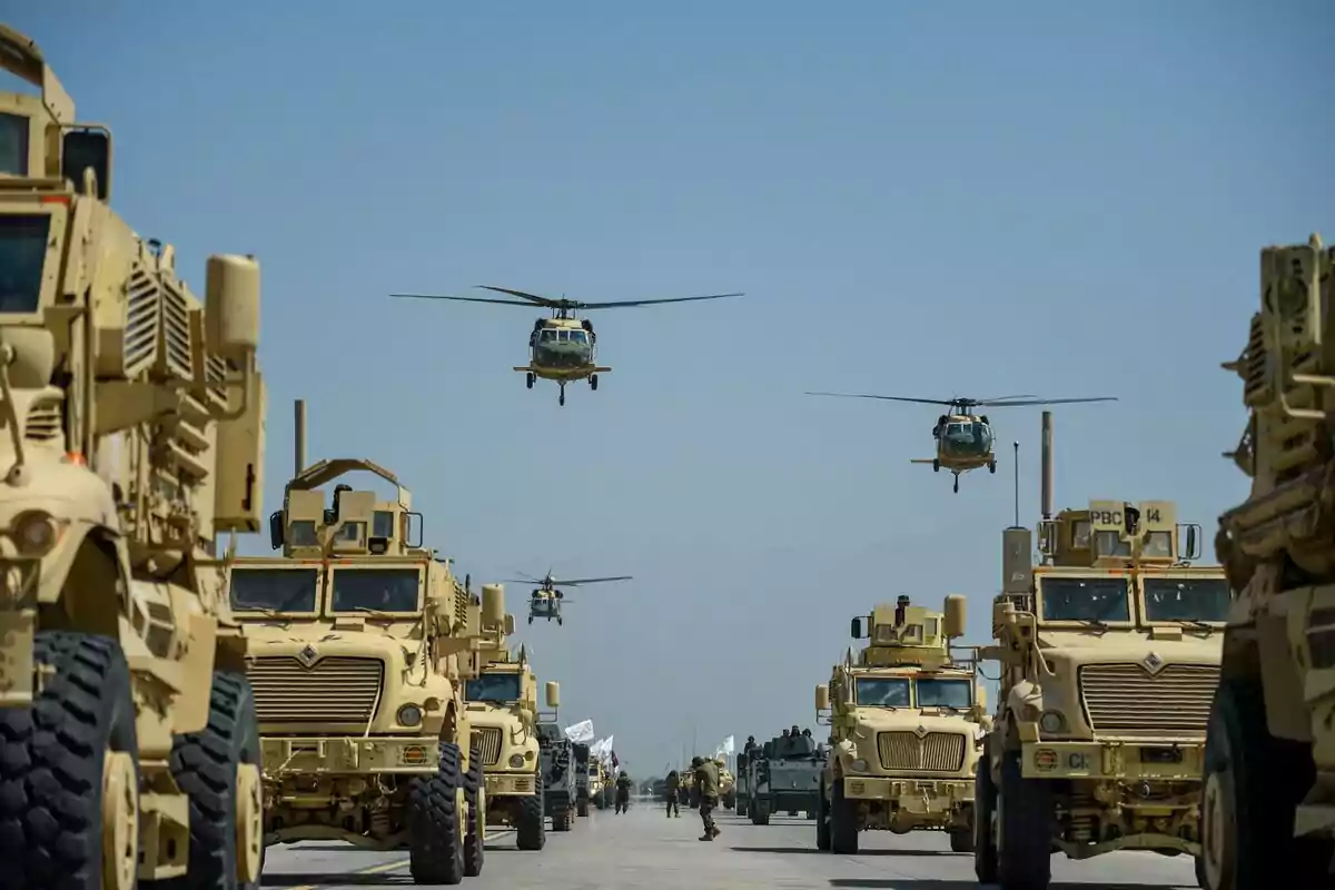 Vehículos militares alineados en una carretera con helicópteros volando sobre ellos bajo un cielo despejado.