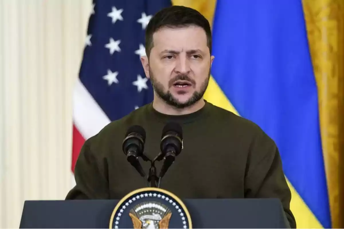 Un hombre hablando en un podio con banderas de fondo.