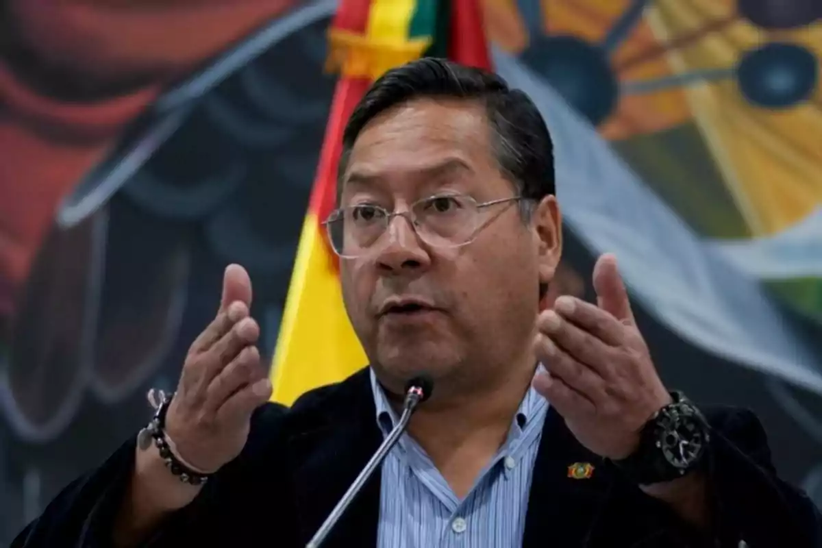 Un hombre hablando en un micrófono con una bandera de fondo.