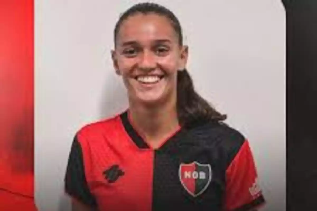 Una persona sonriendo con la camiseta de un equipo de fútbol con los colores rojo y negro.