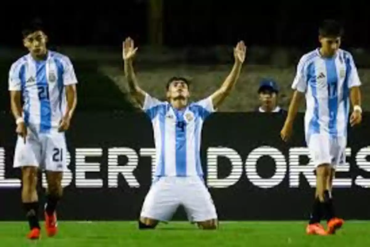 Jugadores de fútbol con uniforme de Argentina en el campo, uno de ellos arrodillado con los brazos levantados.