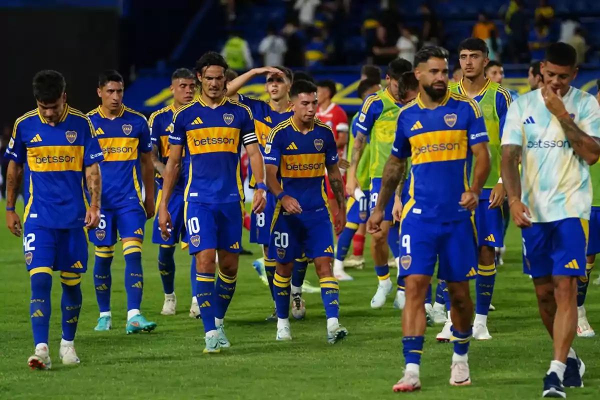 Jugadores de fútbol con uniforme azul y amarillo caminando en el campo después de un partido.