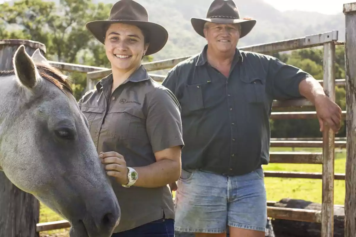 Una mujer y un hombre con sombreros de vaquero posan junto a un caballo en un entorno rural.