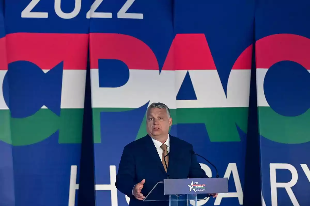 Un hombre hablando en un podio frente a un fondo con letras grandes y coloridas.