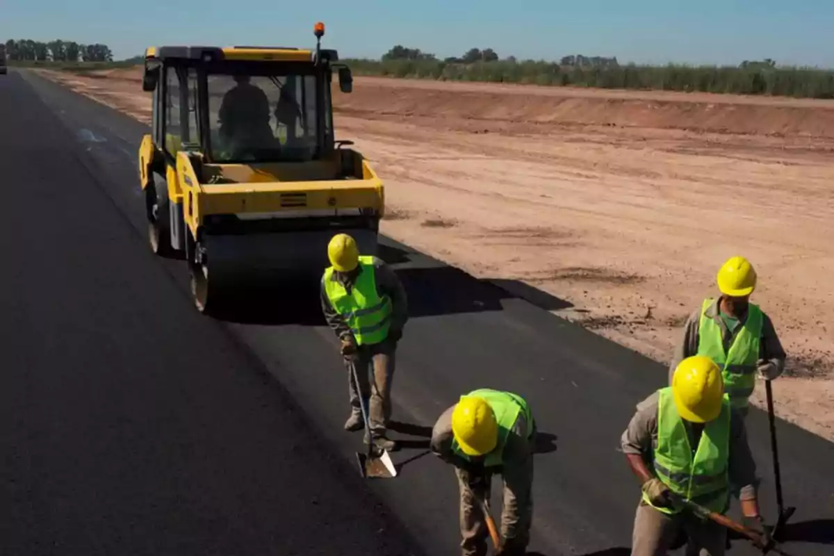 Trabajadores de la construcción pavimentando una carretera con un rodillo compactador y herramientas manuales.