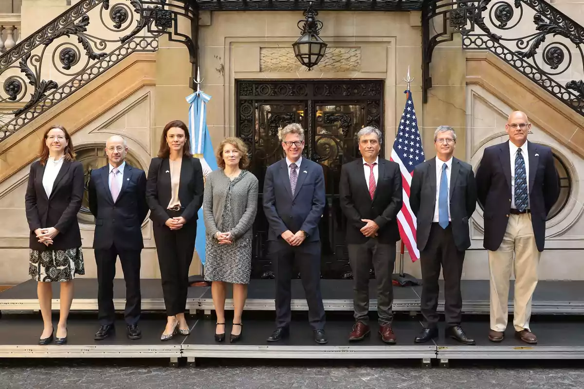 Un grupo de personas posando frente a un edificio con banderas de Argentina y Estados Unidos.