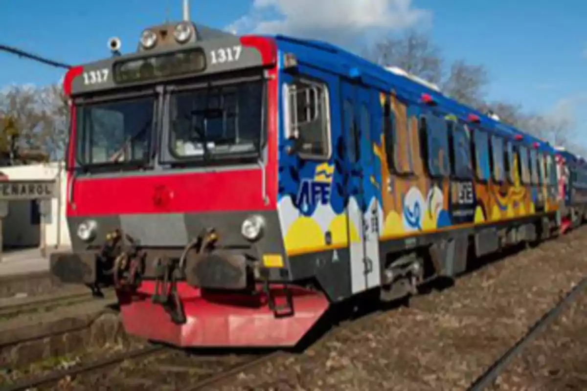 Un tren colorido estacionado en una vía férrea cerca de un edificio que dice 