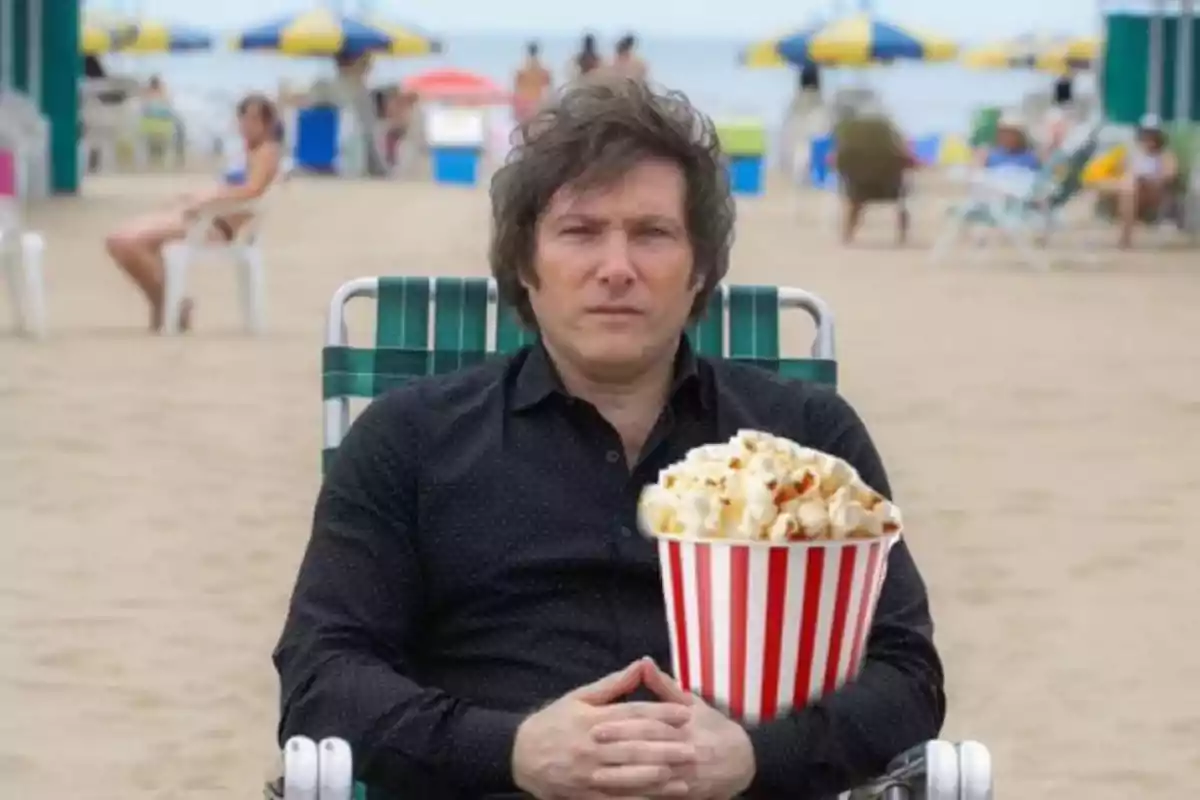 Una persona sentada en una silla de playa sosteniendo un recipiente de palomitas de maíz con un fondo de playa y sombrillas.