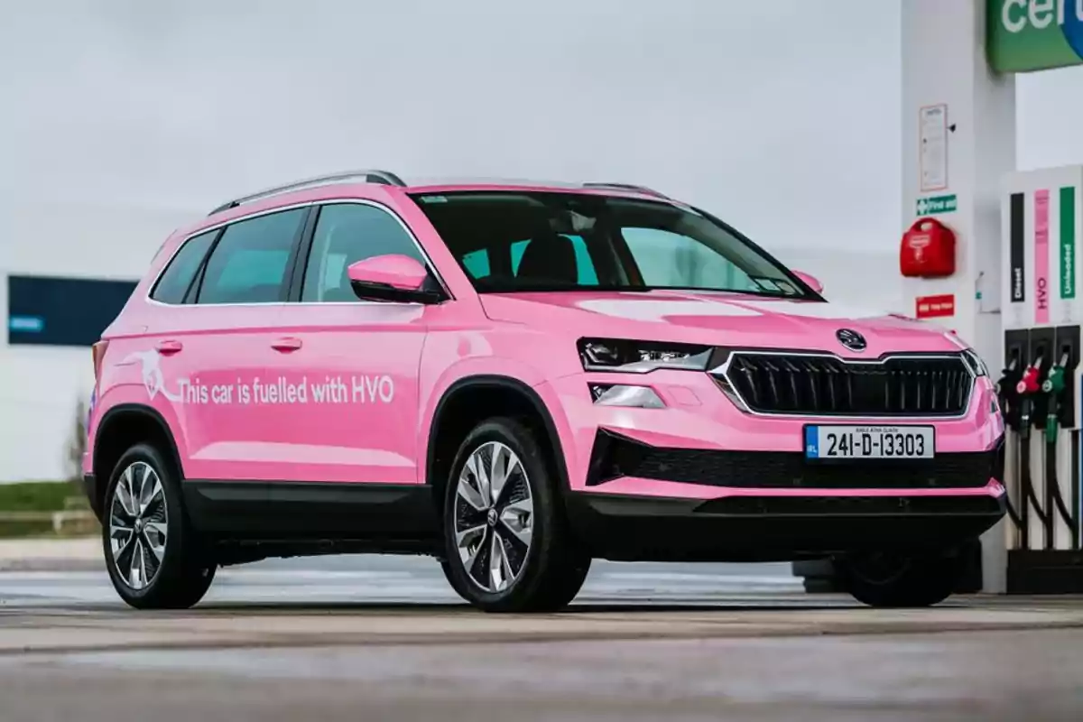 Un coche SUV rosa estacionado en una gasolinera con un letrero que indica que funciona con HVO.