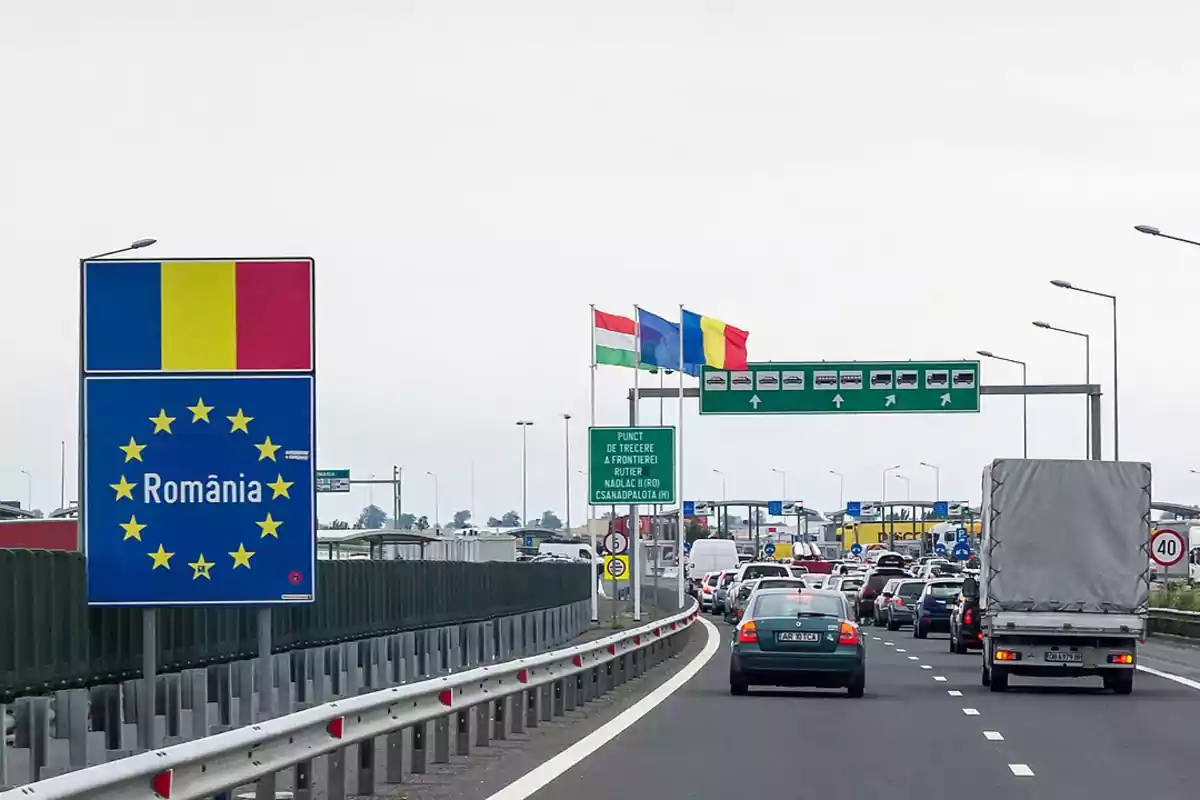 Una carretera con tráfico en la frontera de Rumania, con señales y banderas visibles.