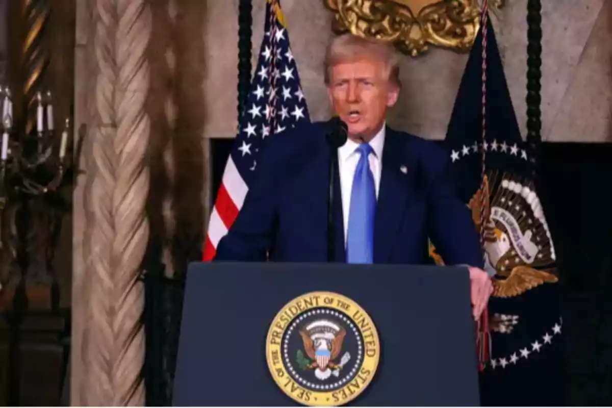 Un hombre de traje azul habla desde un podio con el sello presidencial de Estados Unidos y banderas de fondo.