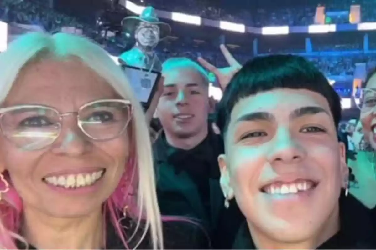 Personas sonriendo y posando para una selfie en un evento con una multitud de fondo.