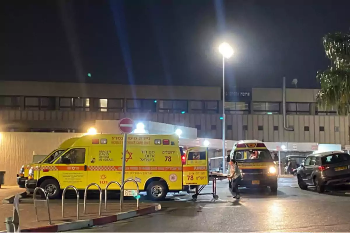 Una ambulancia amarilla estacionada frente a un edificio por la noche con una camilla siendo retirada por una persona.