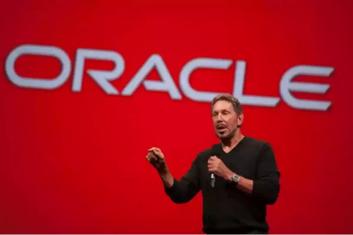 Hombre hablando en un escenario con un micrófono frente a un fondo rojo con el logo de Oracle.