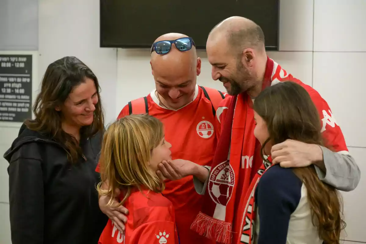 Un grupo de personas sonríe y comparte un momento de alegría, algunas visten camisetas y bufandas rojas.