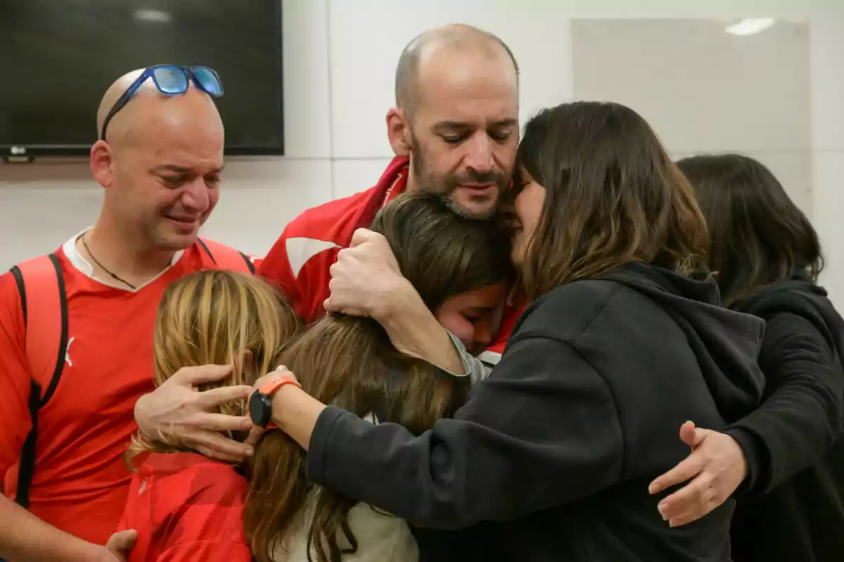 Un grupo de personas se abraza con emoción en un ambiente interior.