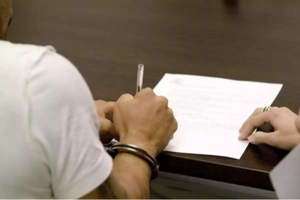 Una persona con esposas firmando un documento en una mesa.