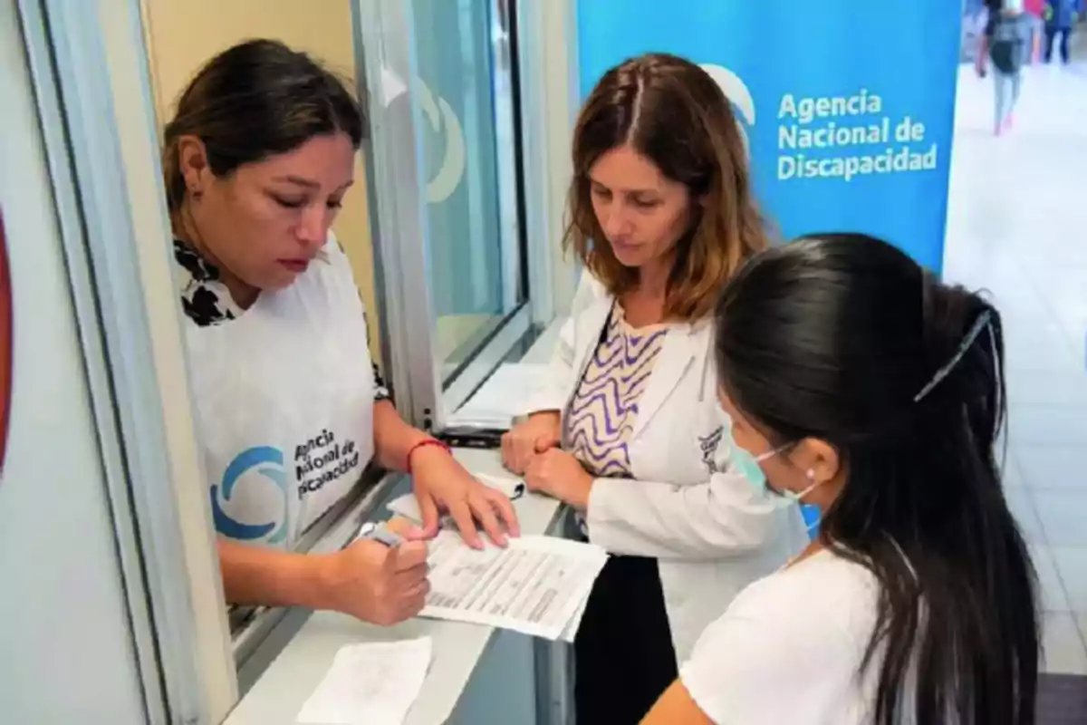 Tres mujeres en una oficina de la Agencia Nacional de Discapacidad revisando documentos.