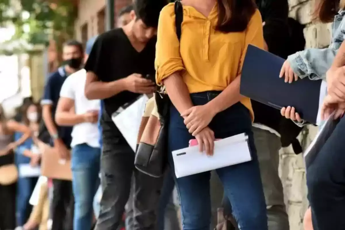 Personas haciendo fila mientras sostienen documentos.