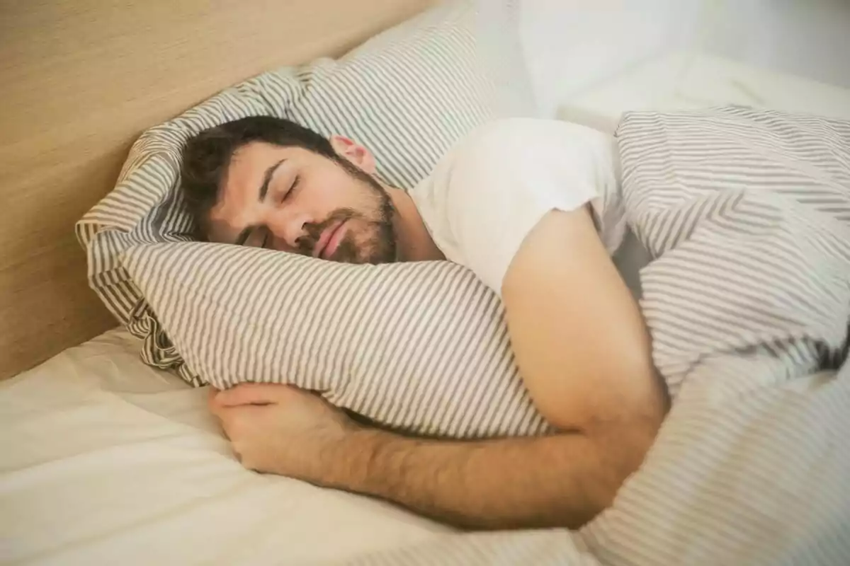 Hombre durmiendo plácidamente en una cama con sábanas a rayas.