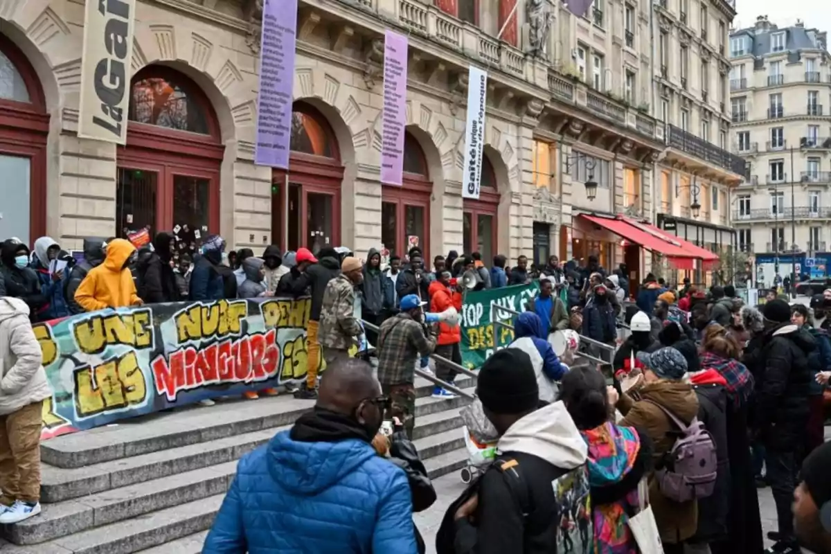 Un grupo de personas se reúne frente a un edificio histórico con pancartas coloridas en una manifestación.