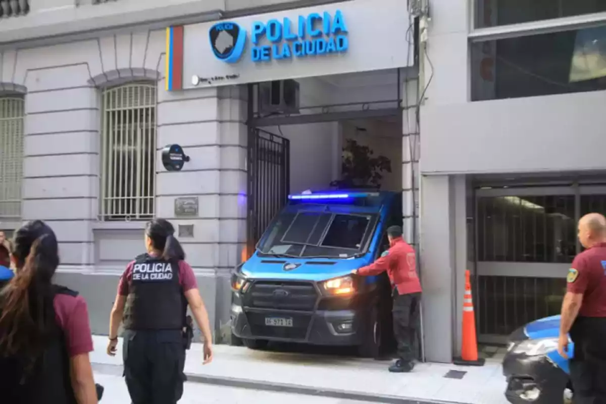 Una camioneta de la policía de la ciudad sale de un edificio mientras varios oficiales observan.