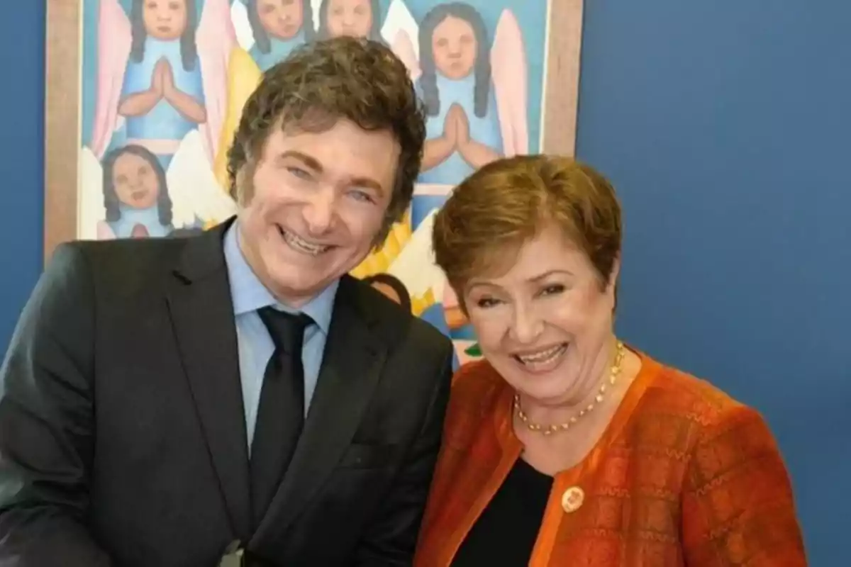 Dos personas sonrientes posan juntas frente a una pintura colorida de ángeles.