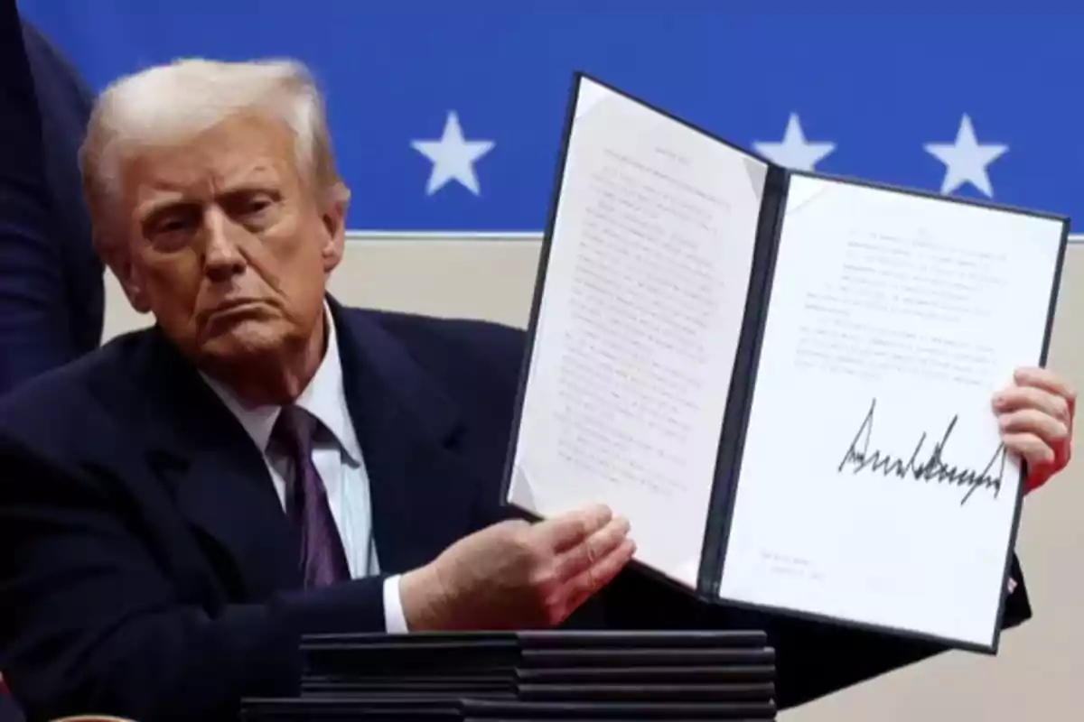 Un hombre de traje oscuro sostiene un documento abierto con una firma visible, frente a un fondo azul con estrellas blancas.