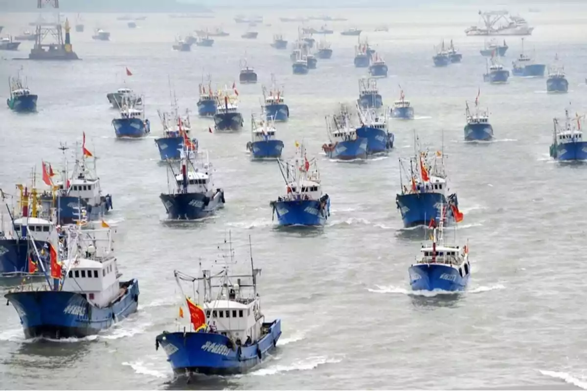 Una flota de barcos pesqueros azules navegando en formación en el mar.