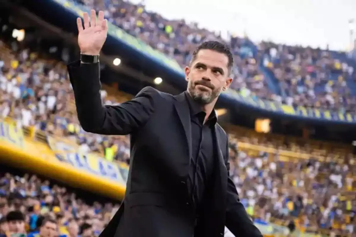 Un hombre con traje negro saluda a una multitud en un estadio de fútbol.