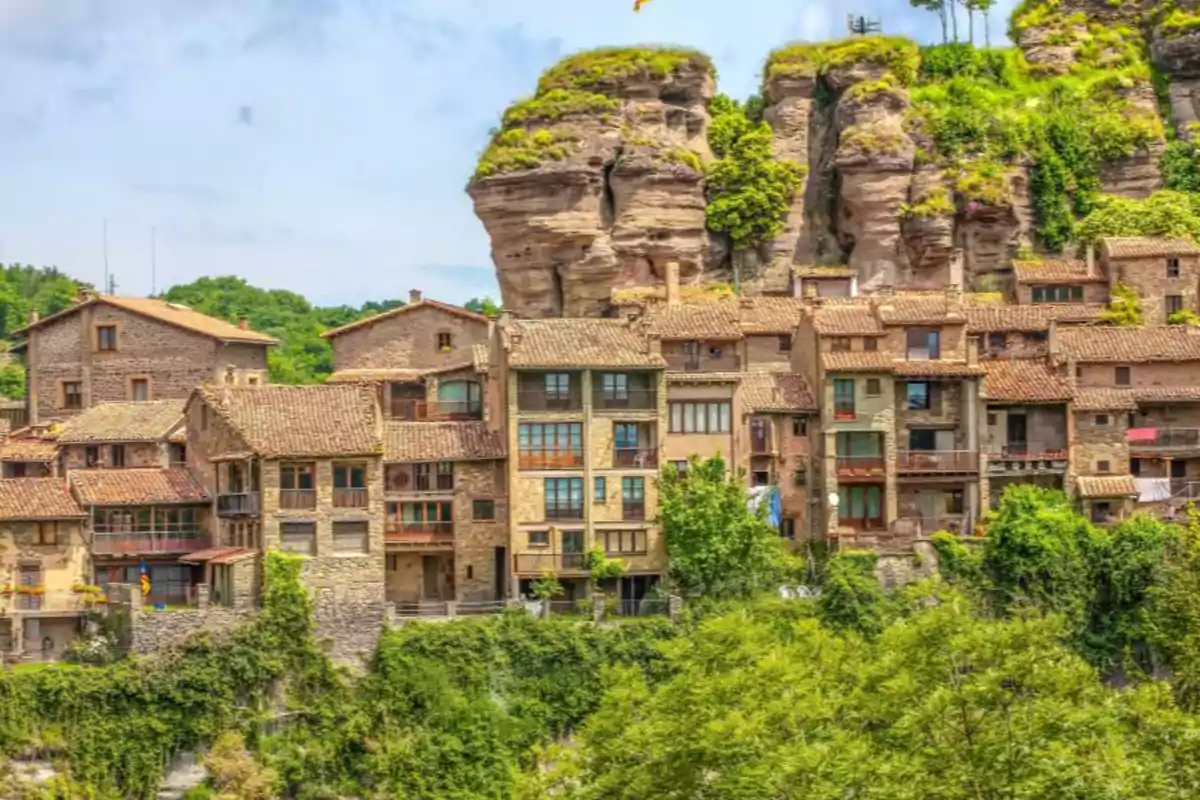 Casas de piedra con tejados de teja roja construidas al pie de un acantilado cubierto de vegetación.