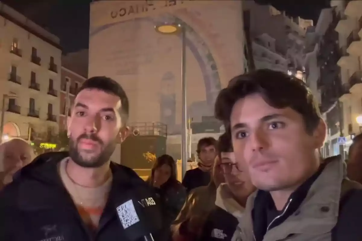 Un grupo de personas en una calle iluminada por la noche con edificios de fondo.