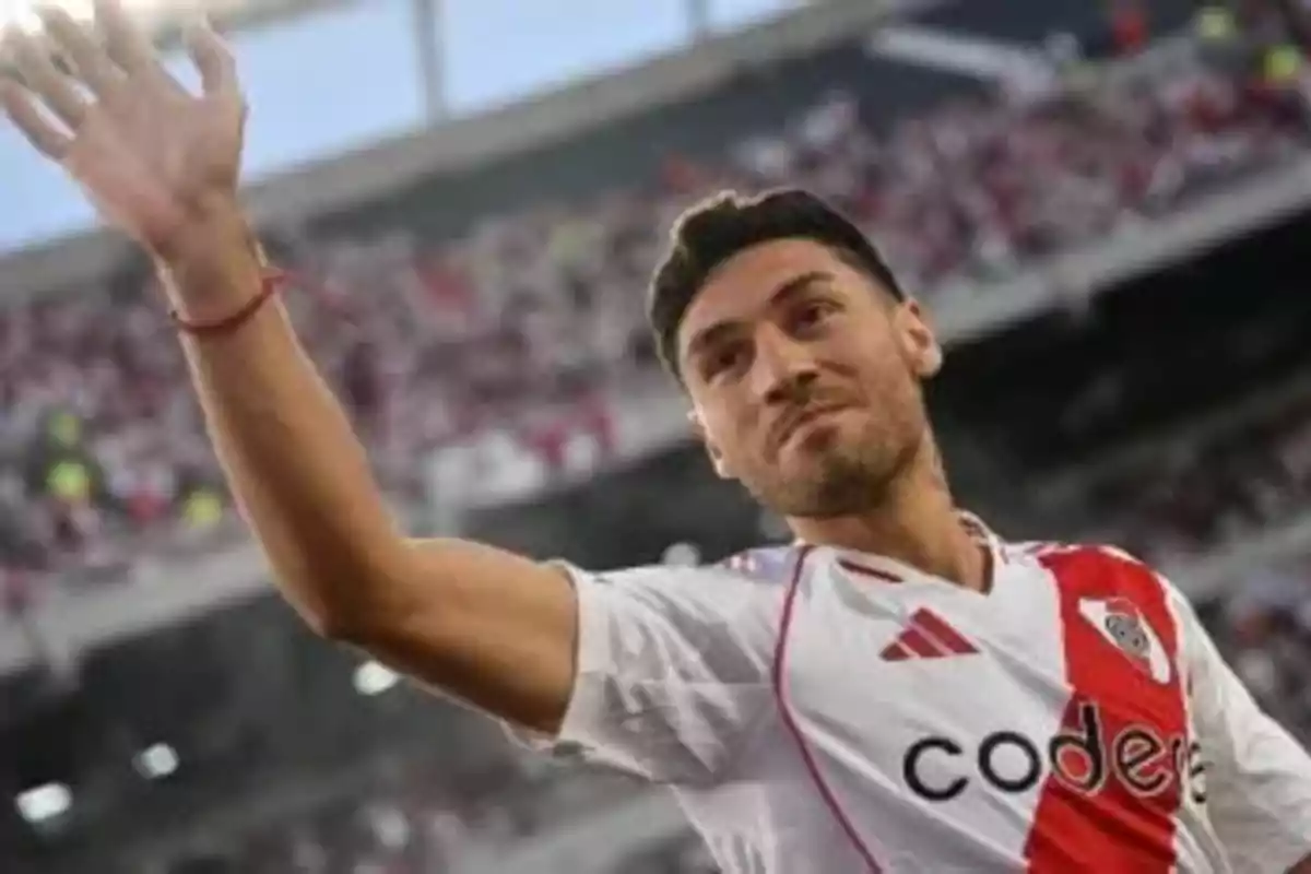 Un jugador de fútbol con uniforme blanco y rojo saluda al público en un estadio lleno.