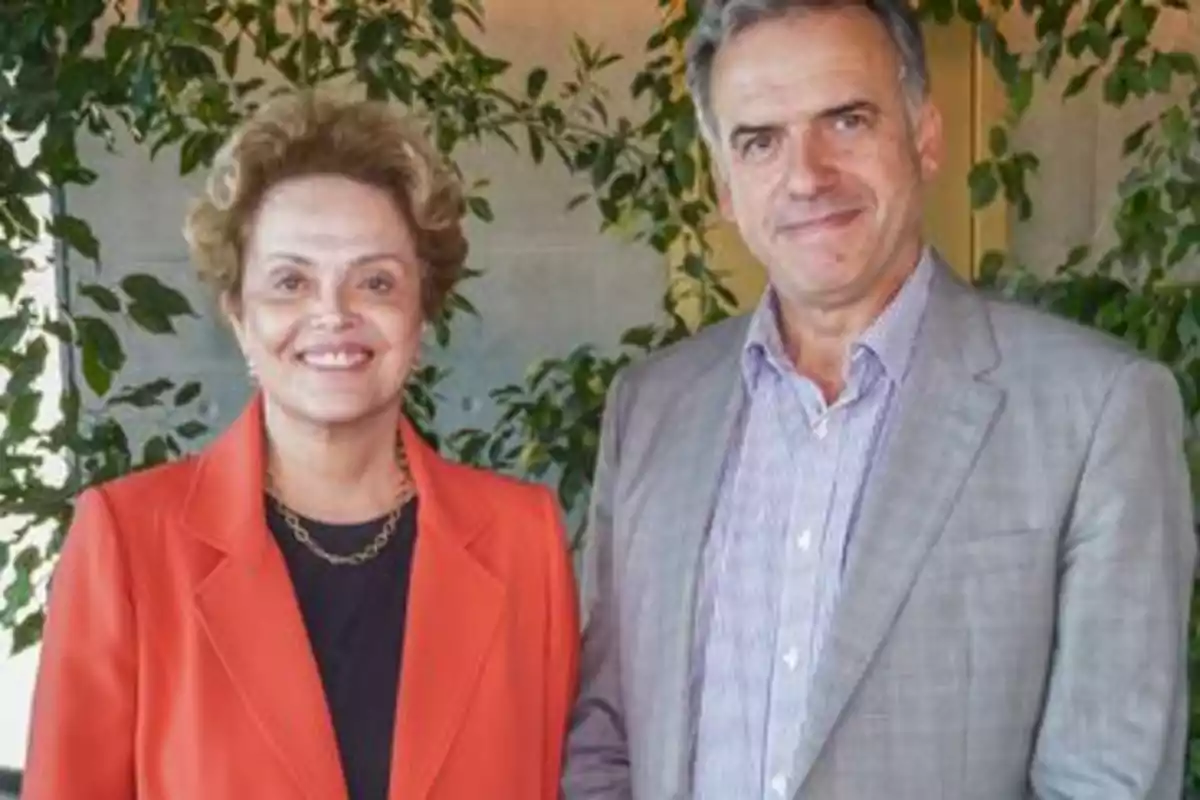 Dos personas posando juntas frente a un fondo de plantas.