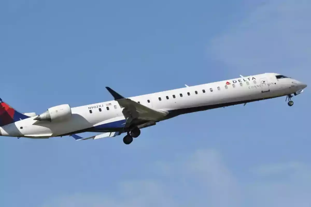 Un avión de pasajeros de Delta Connection en pleno vuelo con el cielo azul de fondo.