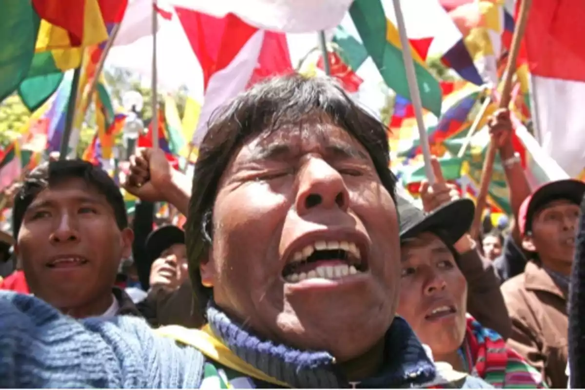 Personas participando en una manifestación con banderas coloridas en el fondo.