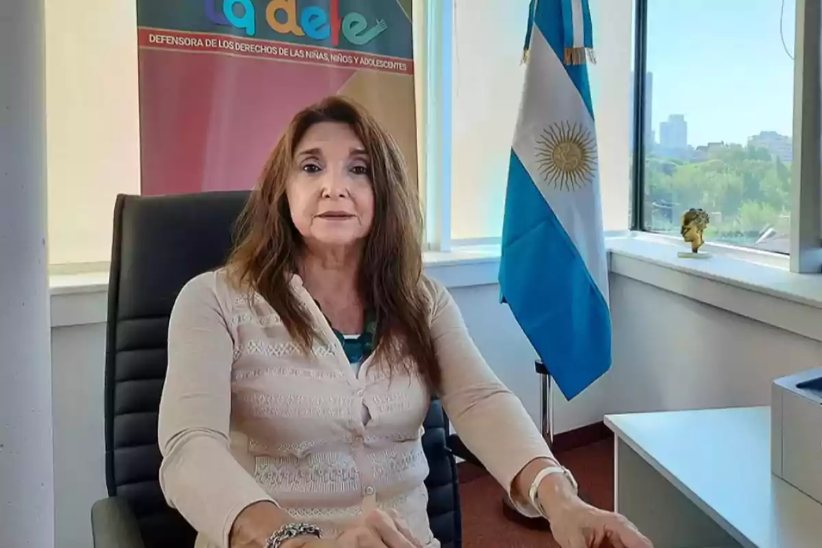 Una mujer sentada en una oficina con una bandera de Argentina al fondo.