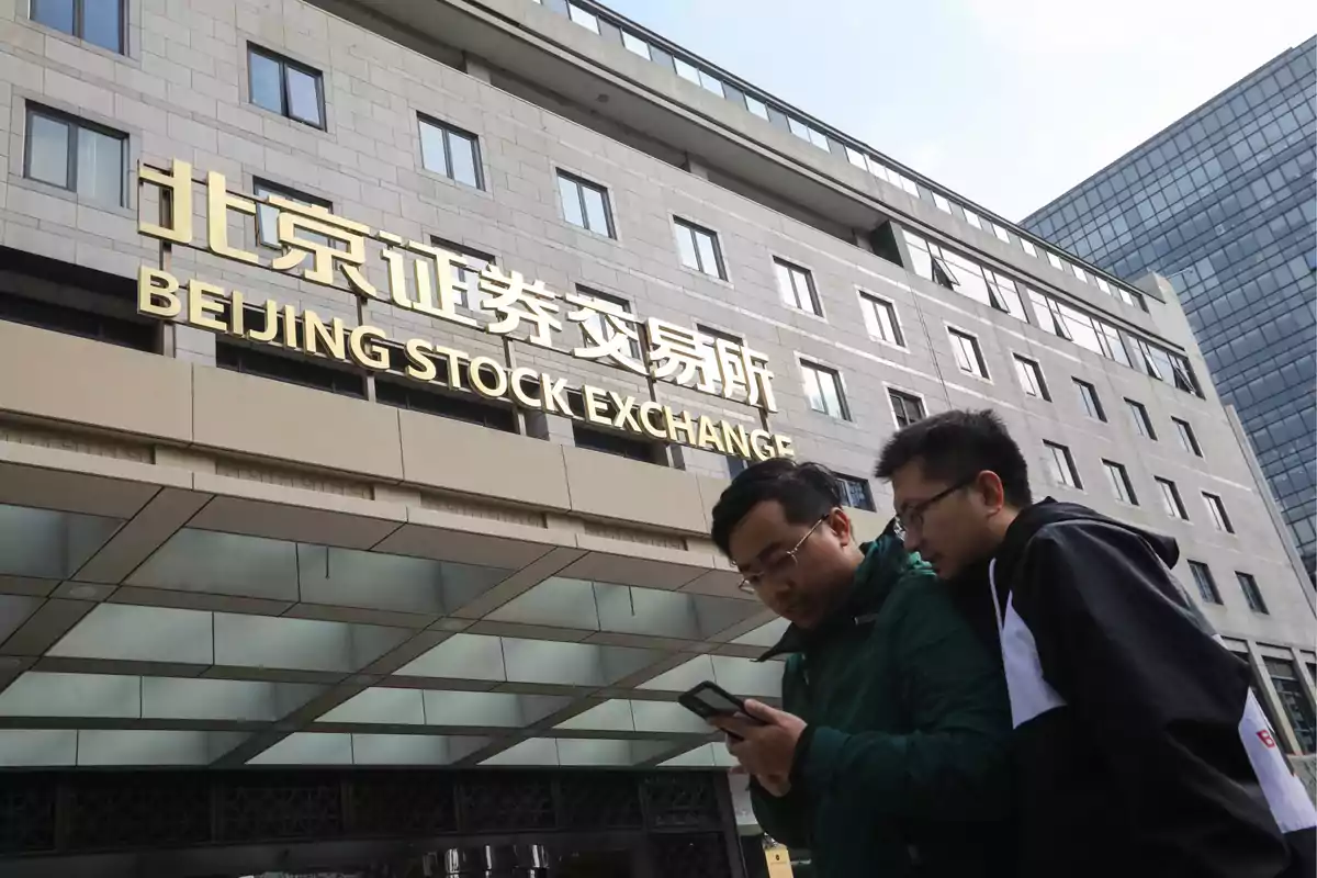 Dos personas mirando un teléfono frente al edificio de la Bolsa de Valores de Beijing.