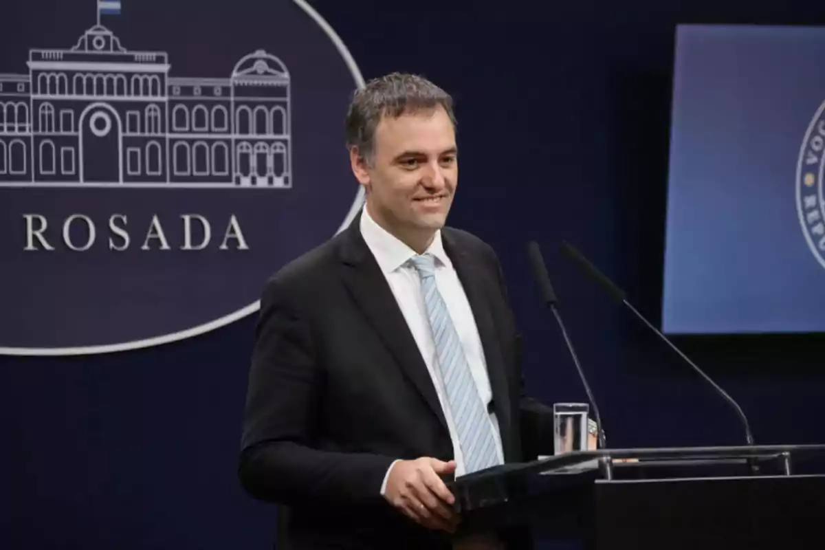 Un hombre de traje y corbata habla en un podio con un fondo que muestra un logotipo de la Casa Rosada.