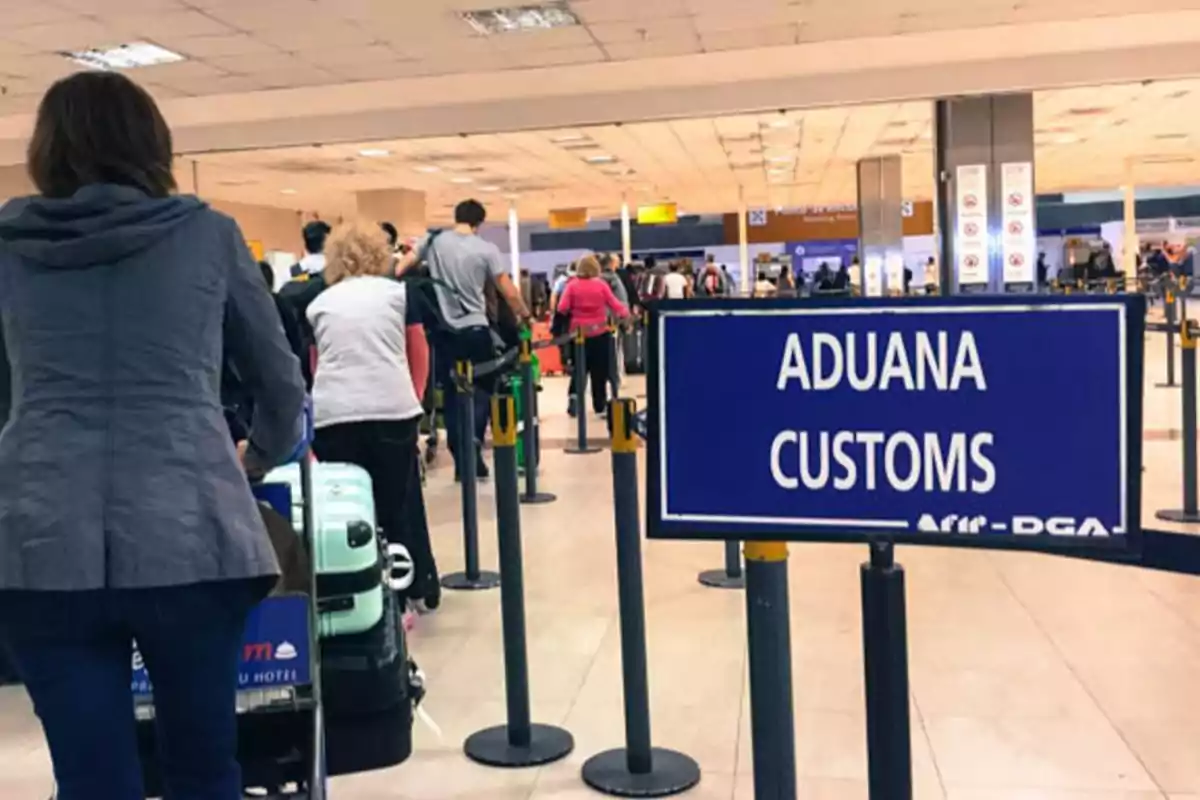 Personas haciendo fila en la aduana de un aeropuerto con un cartel que indica 