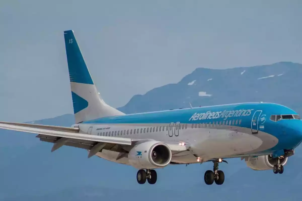 Avión de Aerolíneas Argentinas en vuelo con montañas de fondo.