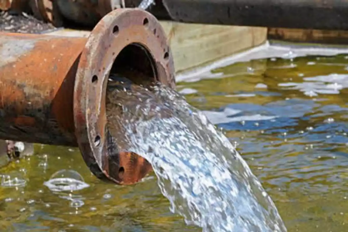 Agua fluyendo de una tubería oxidada hacia un cuerpo de agua.