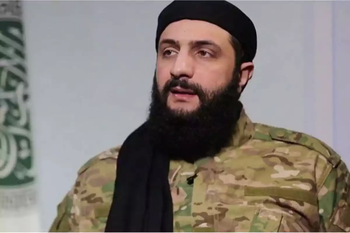 Un hombre con barba y gorra negra vistiendo uniforme militar camuflado.