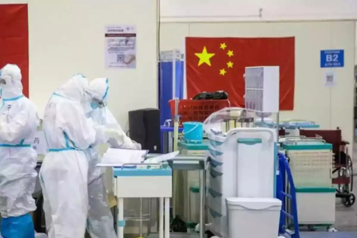 Personal médico con trajes de protección trabajando en un hospital con una bandera de China al fondo por la emergencia de metapneumovirus humano