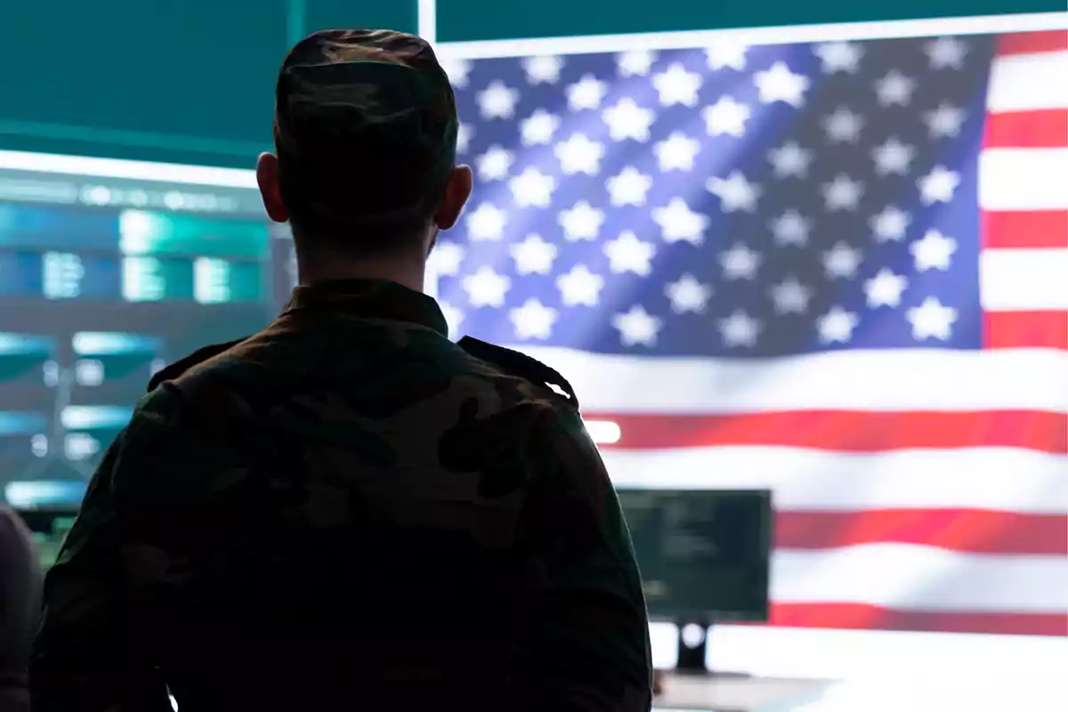 Un soldado de espaldas frente a una pantalla con la bandera de Estados Unidos.