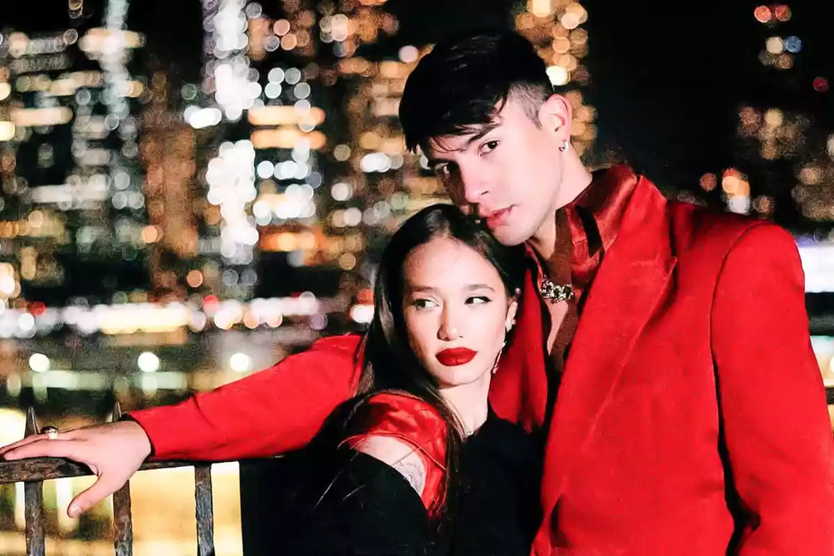 Una pareja vestida de rojo posando frente a un fondo urbano iluminado por la noche.