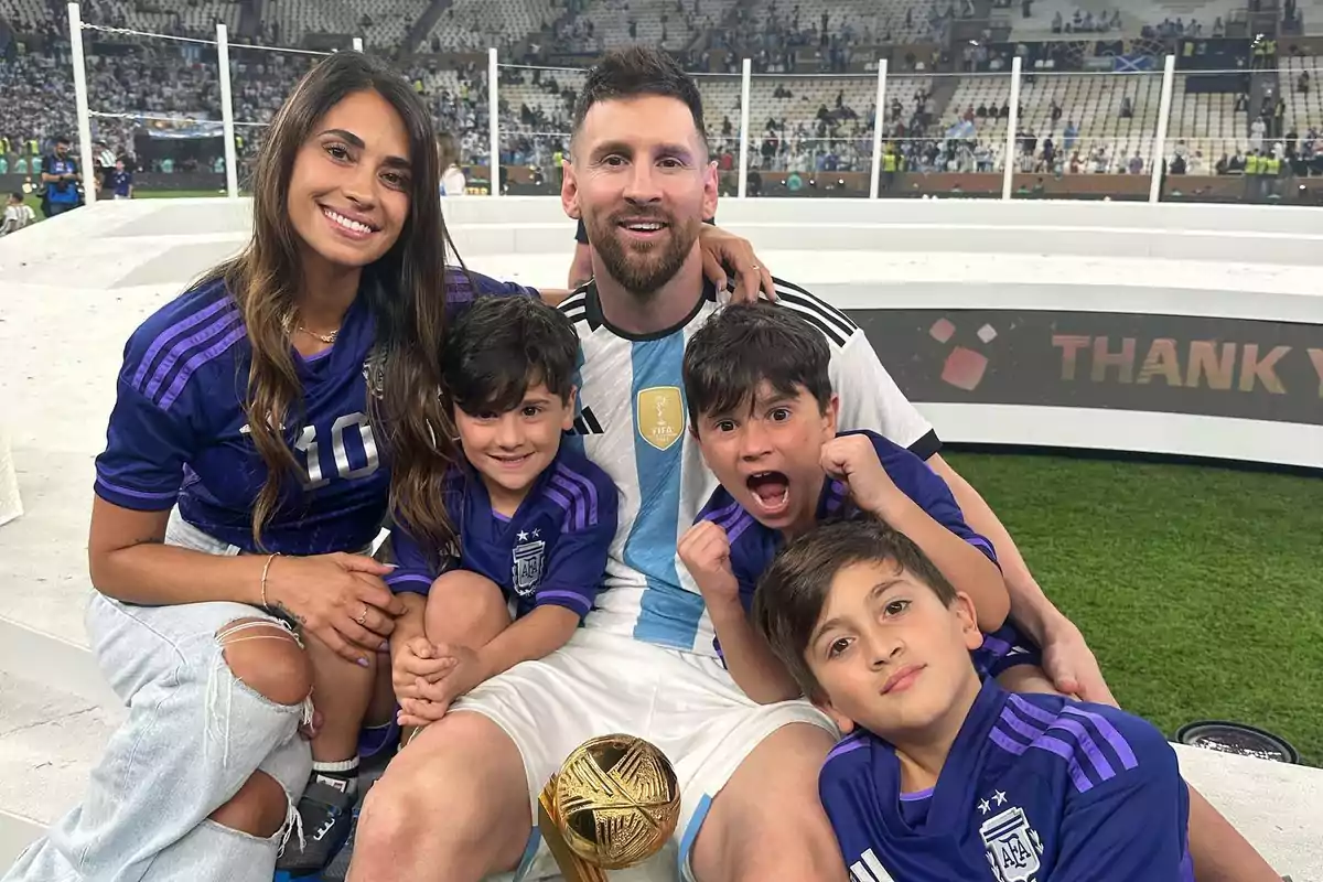 Una familia sonriente posa en un estadio de fútbol, con un trofeo dorado en primer plano.