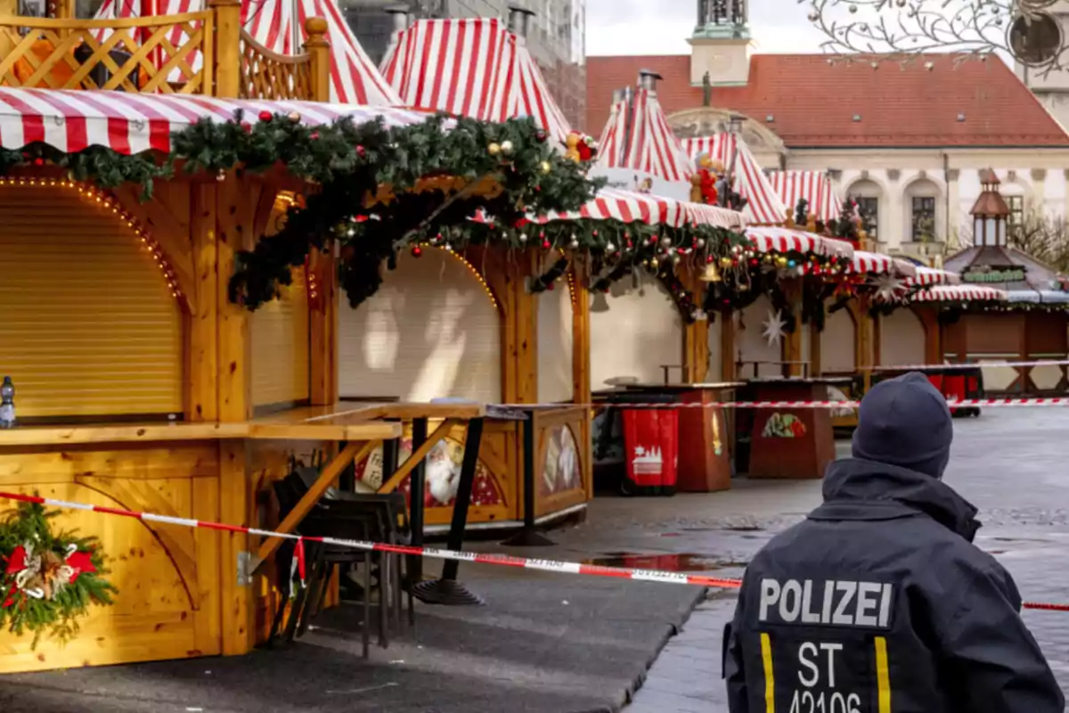 Un mercado navideño con puestos de madera decorados con guirnaldas y luces, acordonado por la policía.