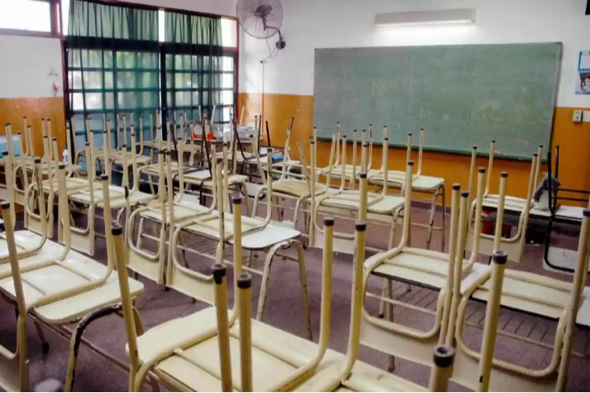 Aula vacía con sillas volteadas sobre los escritorios y un pizarrón al fondo.