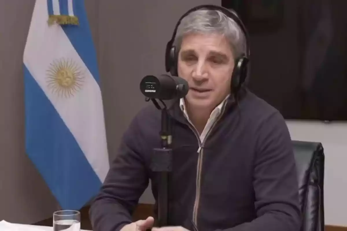 Un hombre con auriculares habla frente a un micrófono en un estudio de grabación, con una bandera de Argentina en el fondo.